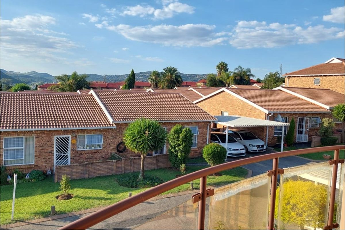 Elevated view of a townhouse complex featuring facebrick exteriors, tiled roofs, private gardens, and covered carport parking.
