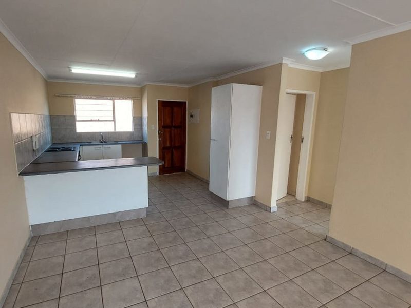An open-plan kitchen and living area featuring tiled flooring, built-in cabinetry, and a breakfast counter, offering a functional and versatile living space.