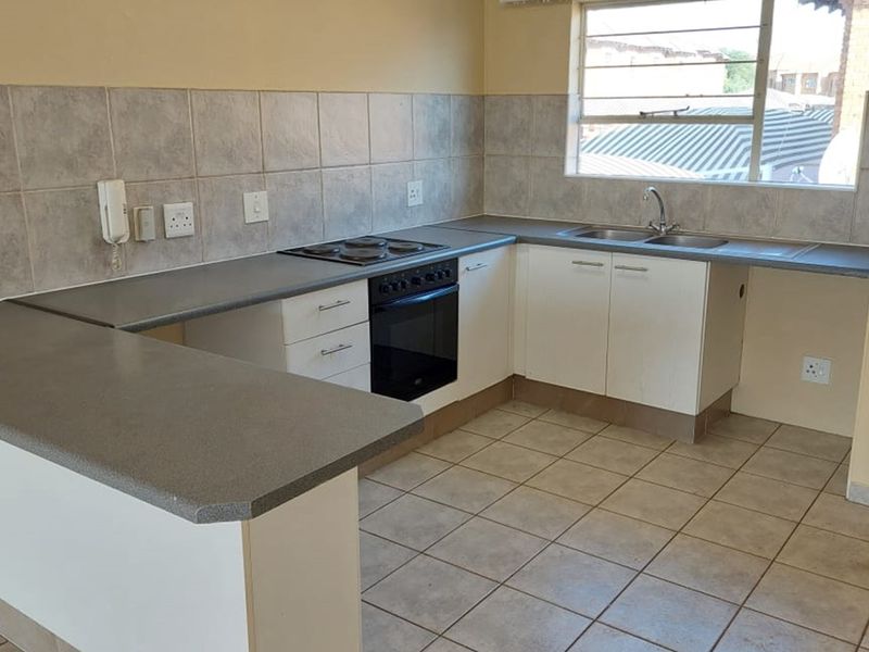 A functional kitchen featuring built-in cabinetry, laminate countertops, an integrated electric oven and hob, and tiled finishes throughout.