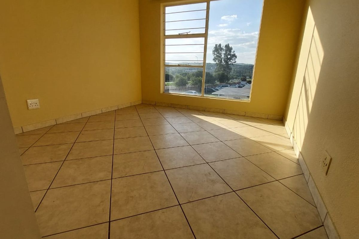 An empty bedroom featuring tiled flooring, tiled skirting, and a large window with security bars, offering natural light and a view.