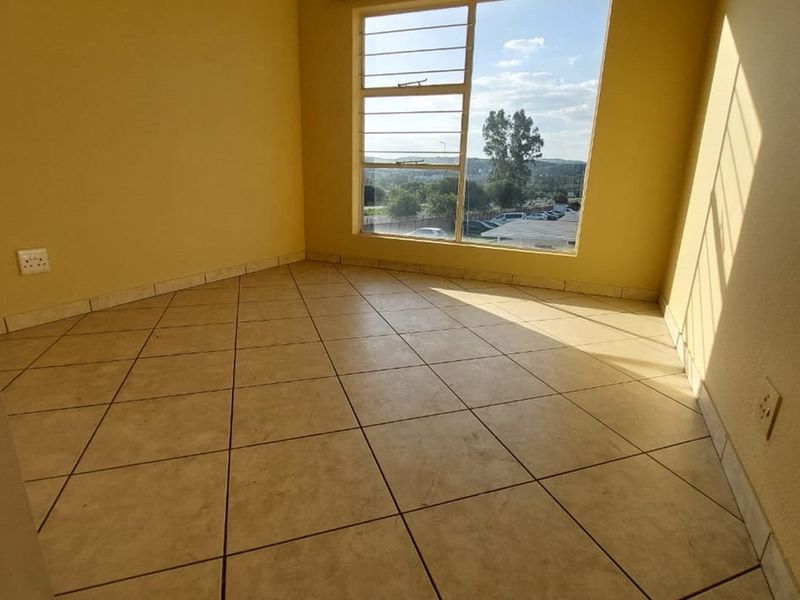 An empty bedroom featuring tiled flooring, tiled skirting, and a large window with security bars, offering natural light and a view.