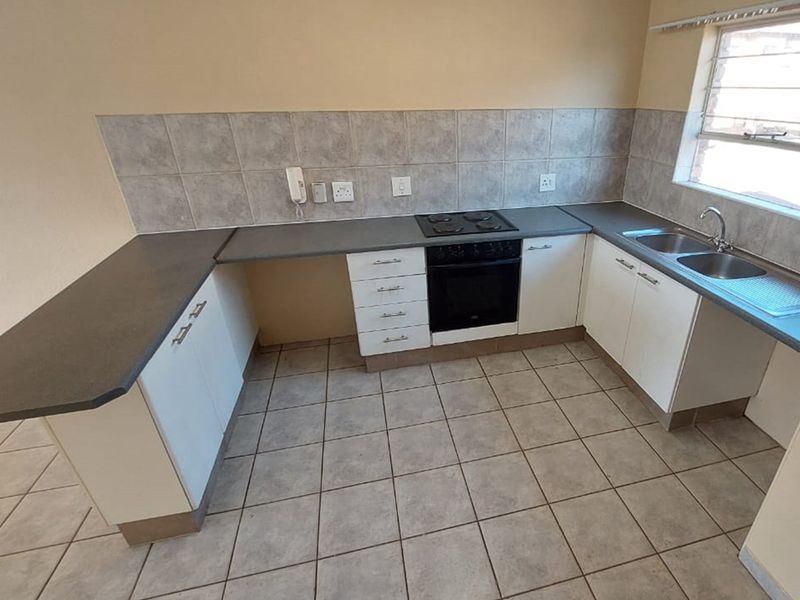 A functional kitchen featuring white cabinetry, dark laminate countertops, a built-in oven with hob, and tiled flooring.