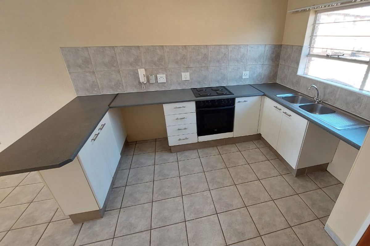 A functional kitchen featuring white cabinetry, dark laminate countertops, a built-in oven with hob, and tiled flooring.
