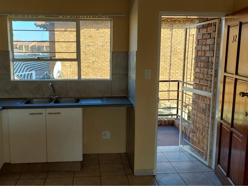 A functional kitchen area featuring a double bowl sink, tiled backsplash, and direct access to an exterior balcony through a security gate.