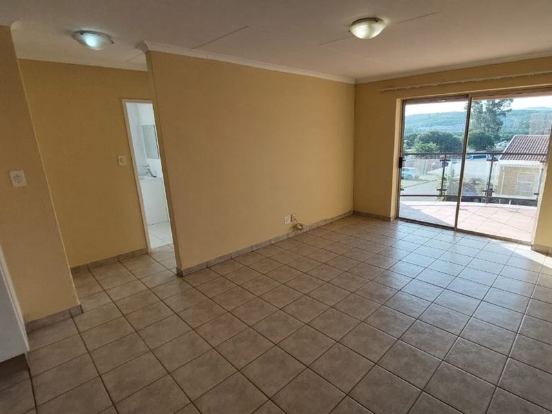 An empty, tiled living room featuring a sliding glass door that opens to an outdoor balcony area, providing natural light and access to views.