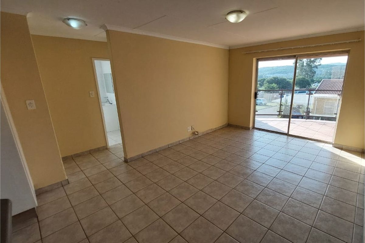 An empty, tiled living room featuring a sliding glass door that opens to an outdoor balcony area, providing natural light and access to views.