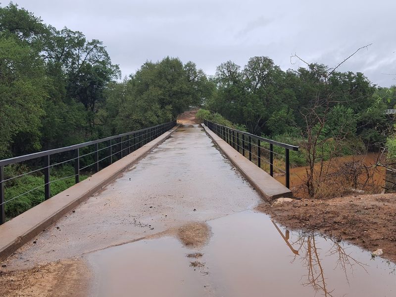 A concrete bridge with metal railings spanning over a natural landscape, providing access to the property.
