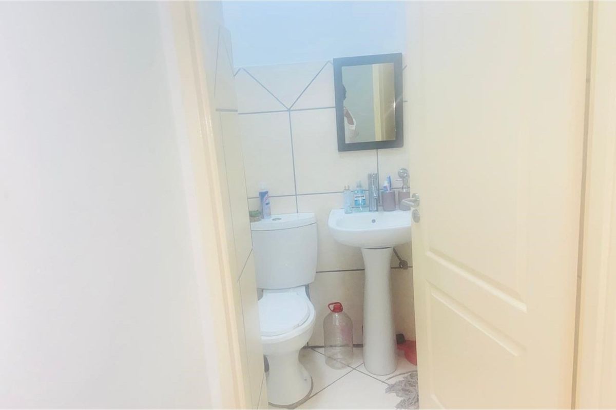 A compact bathroom featuring a pedestal sink, a standard toilet, and tiled walls.