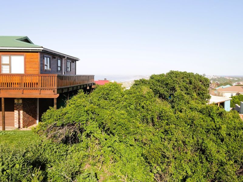 Rear view of a multi-level residential property featuring timber cladding, a raised wooden deck, and integrated garage access, surrounded by established coastal vegetation.