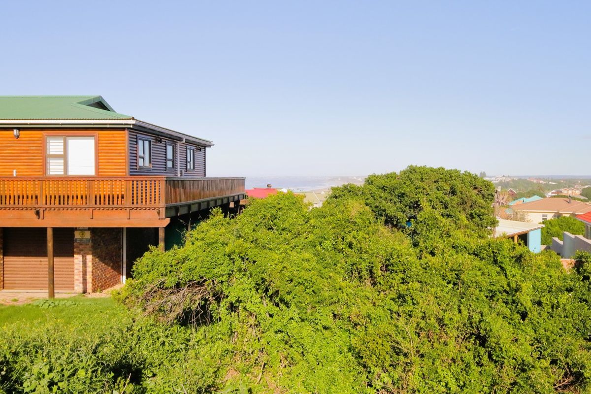 Rear view of a timber-clad residential property featuring a raised deck and garage, overlooking a lush green landscape and distant coastal view.