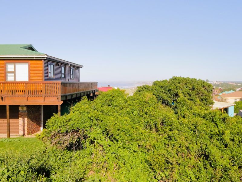 Rear view of a timber-clad residential property featuring a raised deck and garage, overlooking a lush green landscape and distant coastal view.
