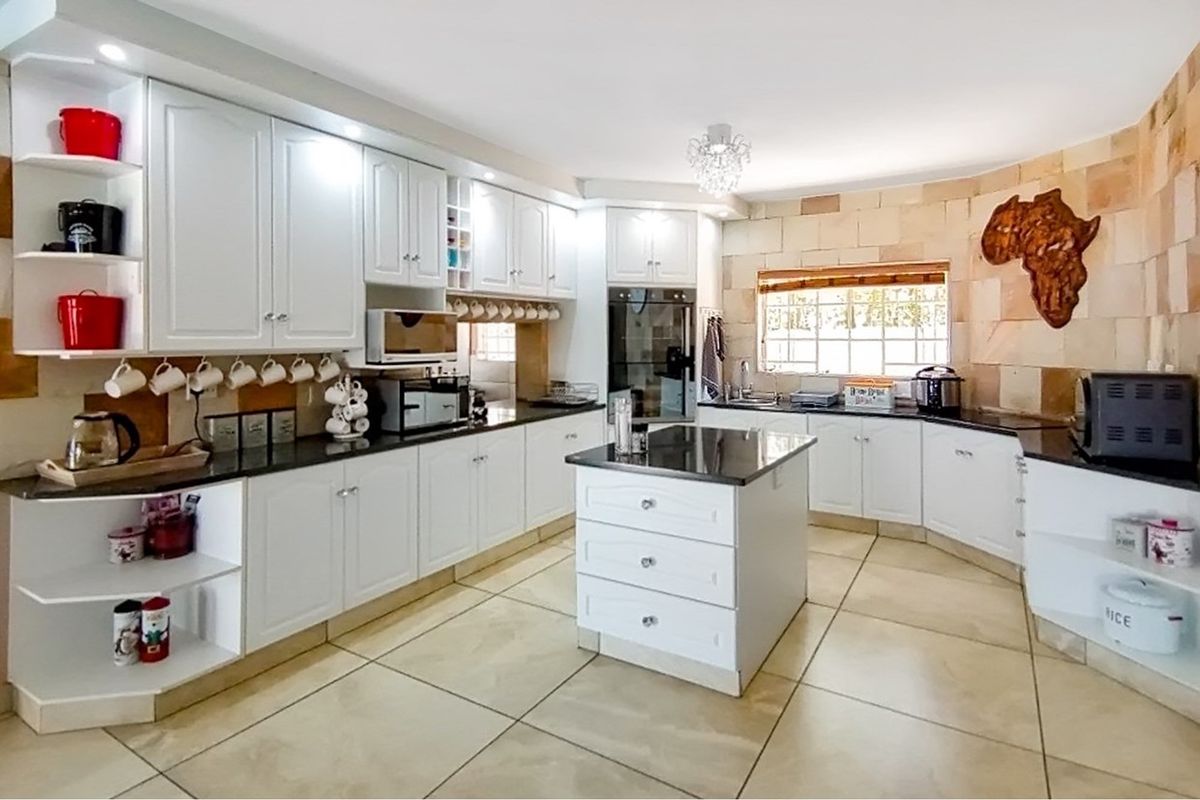 Spacious kitchen featuring white cabinetry, granite countertops, a central island, built-in oven, and stone-clad feature wall with tiled flooring.