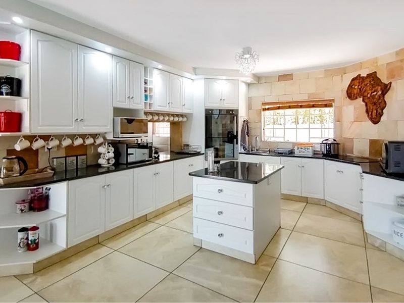 Spacious kitchen featuring white cabinetry, granite countertops, a central island, built-in oven, and stone-clad feature wall with tiled flooring.