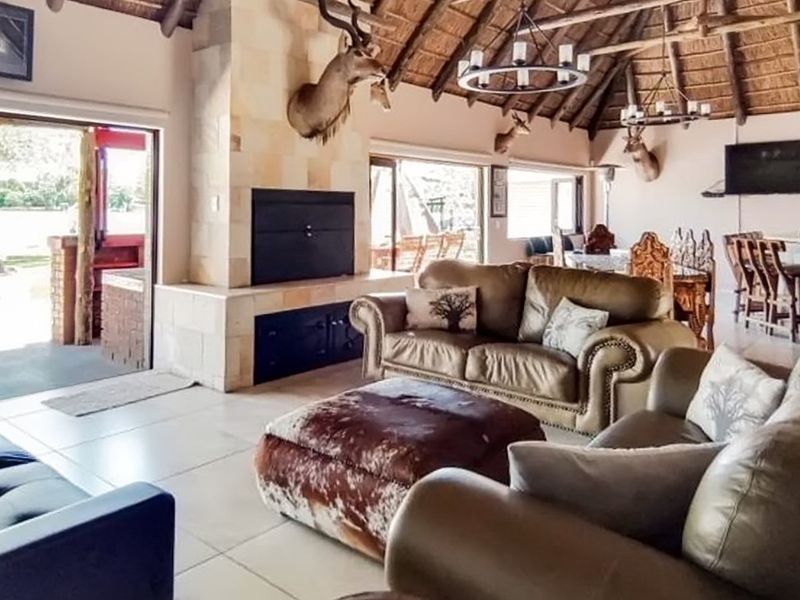 Spacious open-plan living area featuring a stone-clad fireplace, high thatched ceiling with exposed beams, and large sliding doors leading to an outdoor patio.