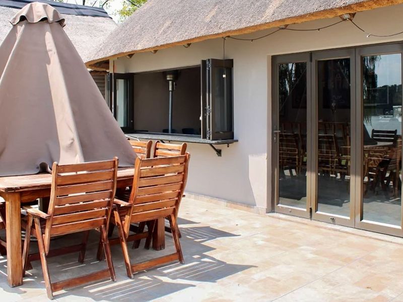 Covered patio area featuring a thatched roof, tiled flooring, and folding glass doors providing seamless access to the interior living space.