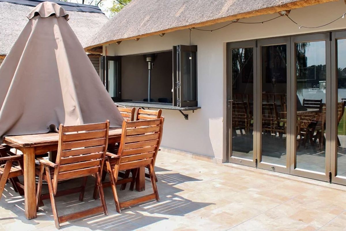 Covered patio area featuring a thatched roof, tiled flooring, and folding glass doors providing seamless access to the interior living space.