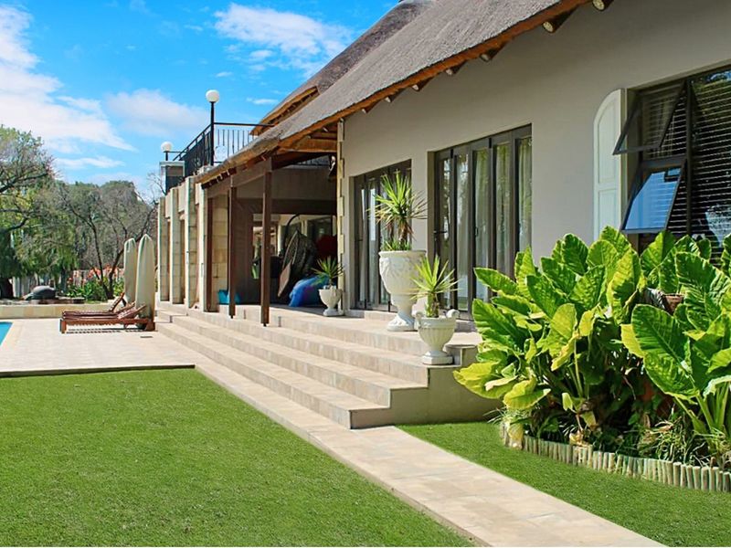 Spacious rear patio area featuring tiled flooring, thatched roof overhang, and direct access to the swimming pool and landscaped garden.