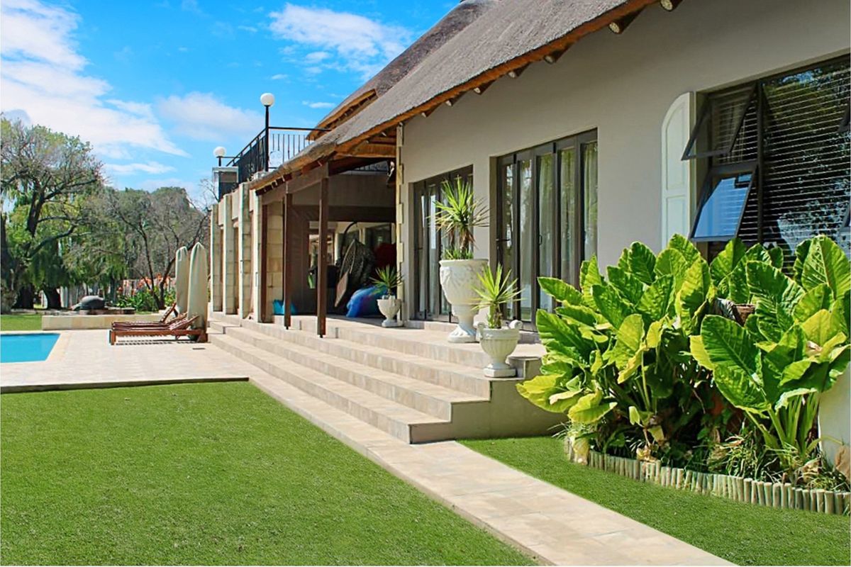 Spacious rear patio area featuring tiled flooring, thatched roof overhang, and direct access to the swimming pool and landscaped garden.