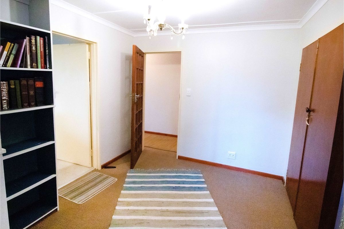 A neutral bedroom featuring carpeted flooring, built-in cabinetry, and access to adjacent rooms through internal doorways.