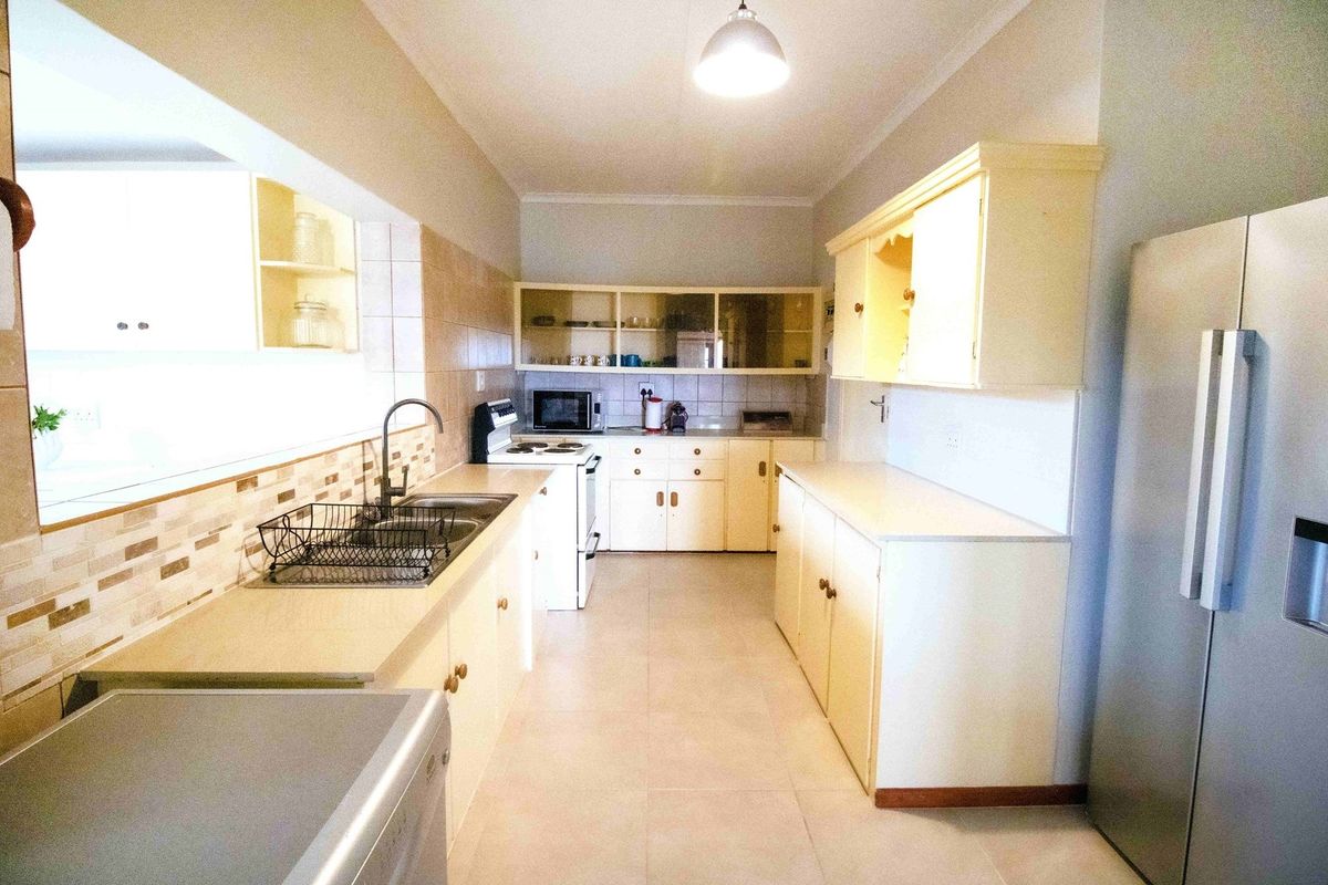 A functional kitchen featuring light-toned cabinetry, tiled backsplash, double basin sink, and tiled flooring, offering a practical layout for daily meal preparation.