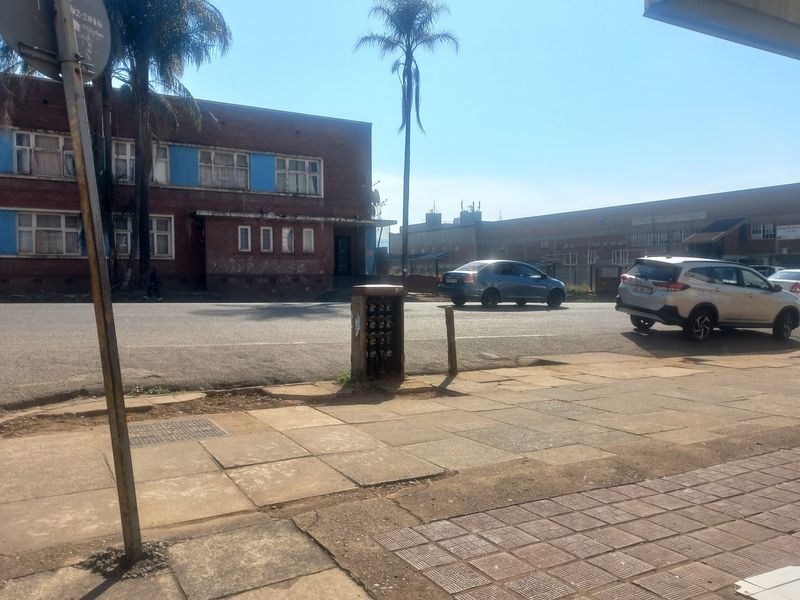 Street view showing the exterior of a brick apartment building with adjacent sidewalk and utility infrastructure.