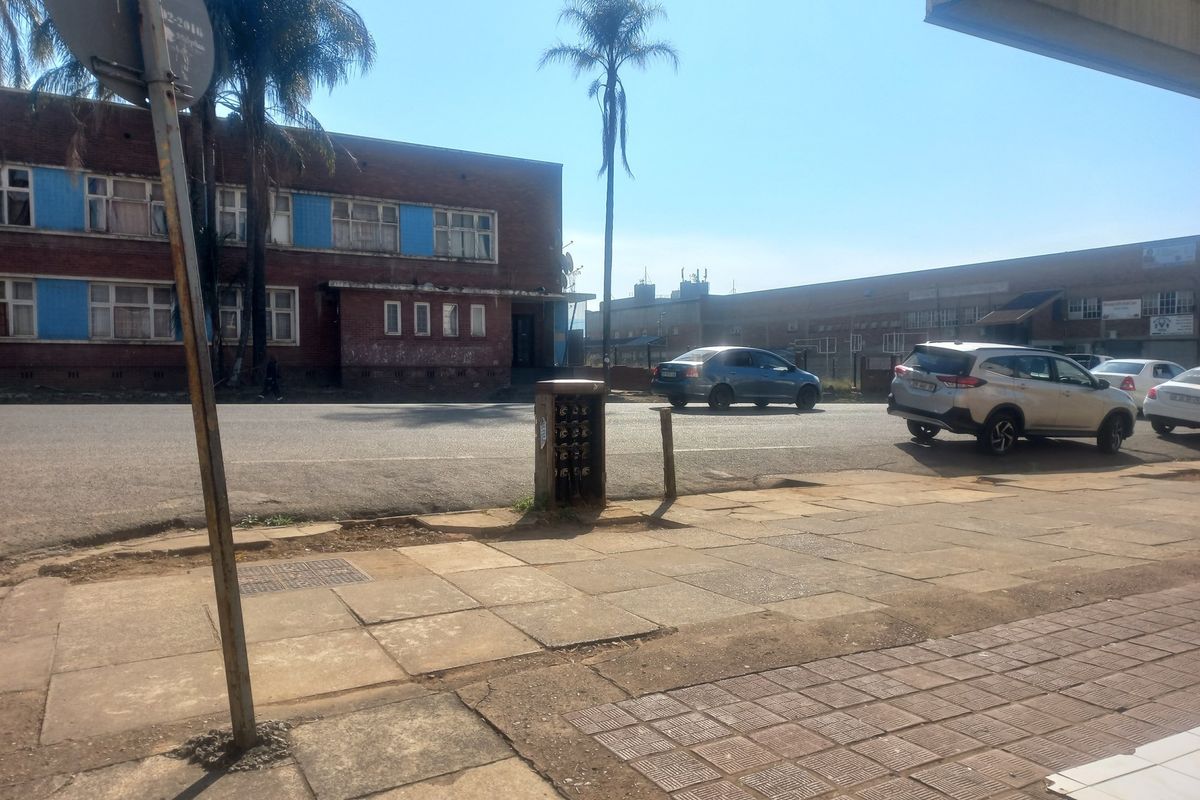Street view showing the exterior of a brick apartment building with adjacent sidewalk and utility infrastructure.