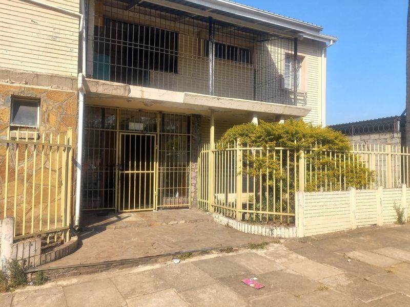 Front exterior view of the apartment building featuring security gates, stone cladding, and a balcony, showing signs of wear and aging.