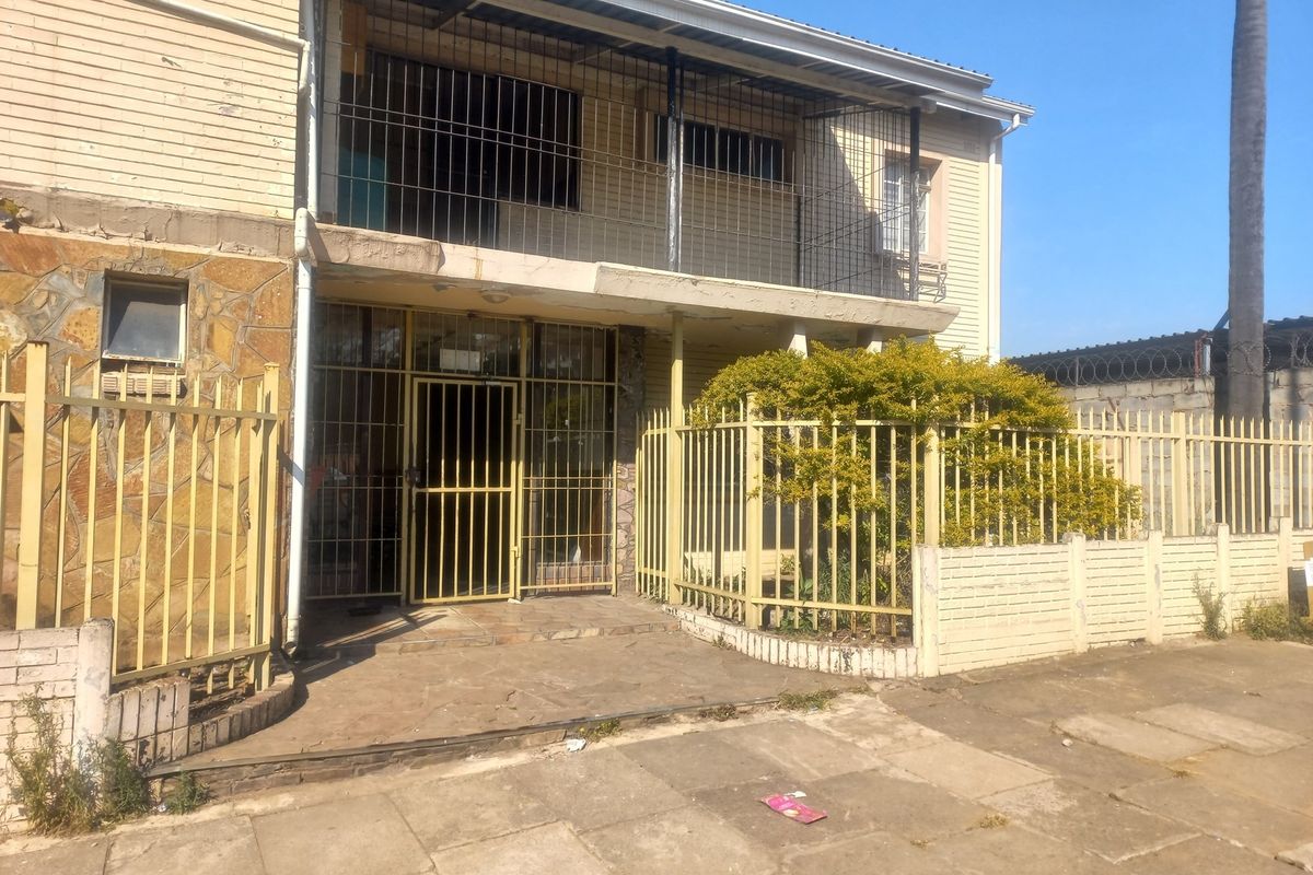 Front exterior view of the apartment building featuring security gates, stone cladding, and a balcony, showing signs of wear and aging.