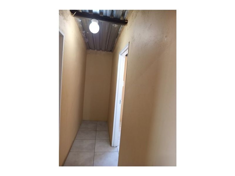 A narrow hallway featuring tiled flooring and an unfinished corrugated metal ceiling with exposed lighting.