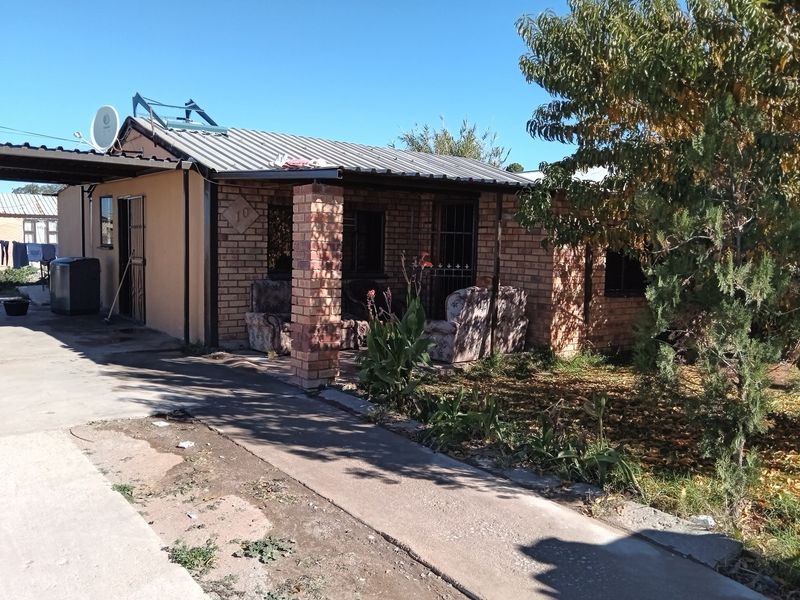 Front view of a single-story brick house featuring a covered porch, corrugated metal roof with solar water heater, and a concrete driveway.
