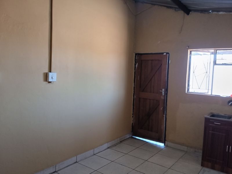 A basic, empty kitchen area featuring tiled flooring, a single sink unit with base cabinetry, and direct access to an exterior door.
