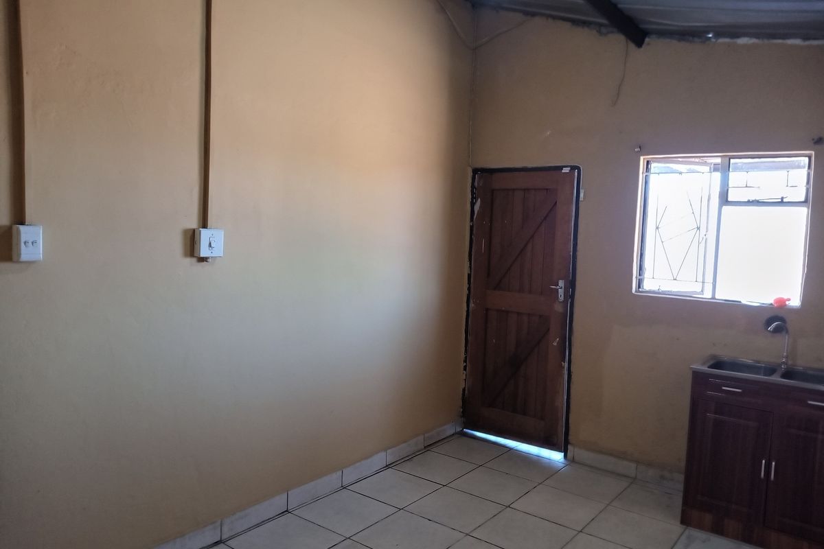A basic, empty kitchen area featuring tiled flooring, a single sink unit with base cabinetry, and direct access to an exterior door.