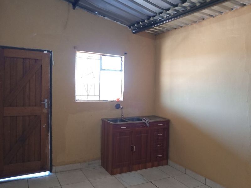 A basic kitchen area featuring a double bowl sink with built-in cabinetry, tiled flooring, and an exposed corrugated metal ceiling.