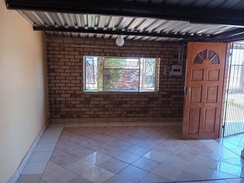An empty garage space featuring exposed brick walls, tiled flooring, and a corrugated metal ceiling with direct access to the exterior.
