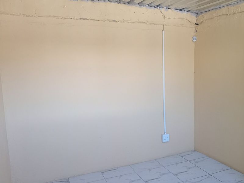An empty room featuring tiled flooring, surface-mounted electrical wiring, and a corrugated metal ceiling, requiring cosmetic updates and finish improvements.