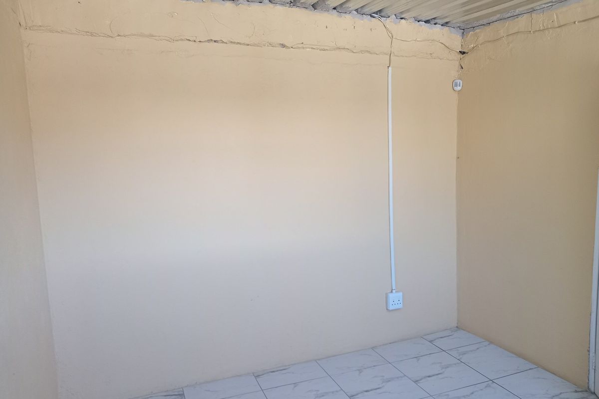 An empty room featuring tiled flooring, surface-mounted electrical wiring, and a corrugated metal ceiling, requiring cosmetic updates and finish improvements.