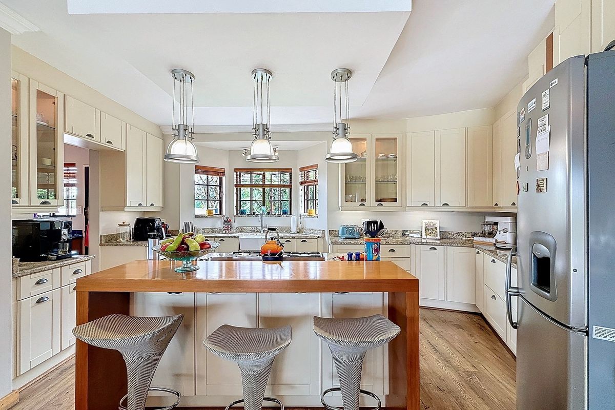 A well-appointed kitchen featuring cream cabinetry, granite countertops, a central island with a wooden breakfast bar, and pendant lighting.