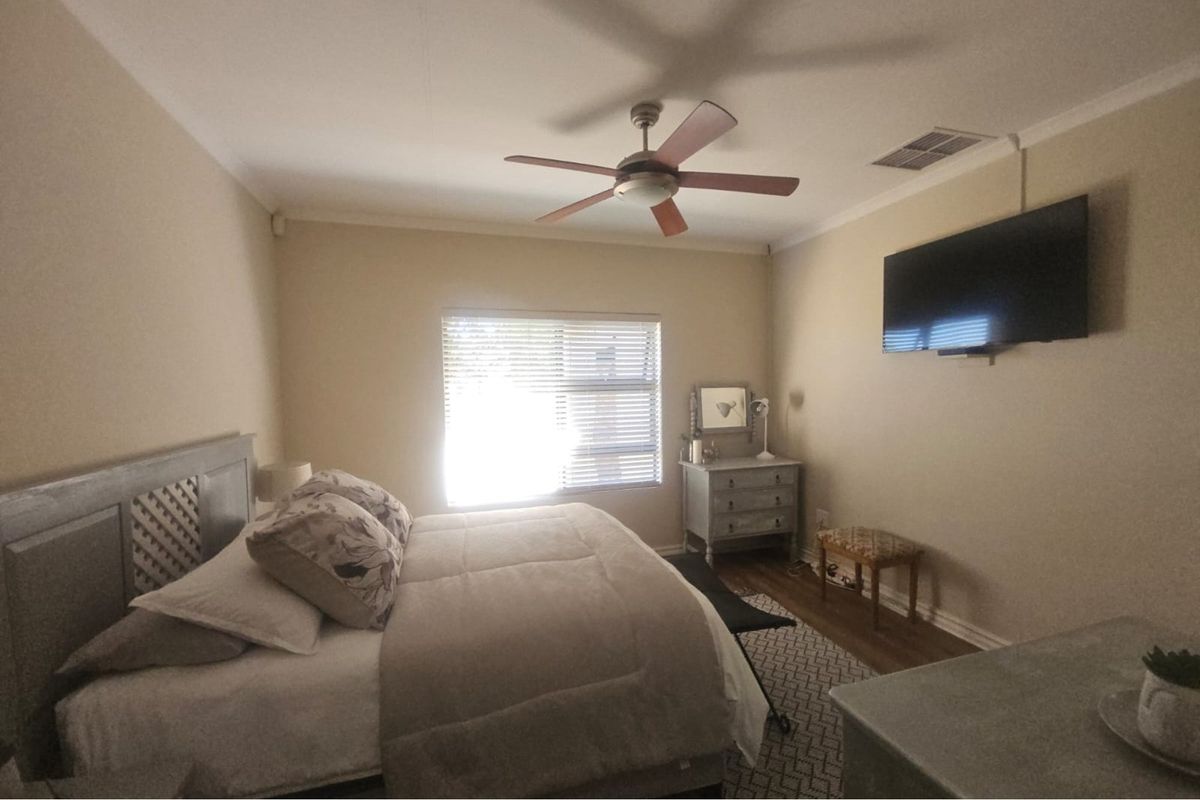 A well-lit bedroom featuring a ceiling fan, central air conditioning vent, and horizontal window blinds.