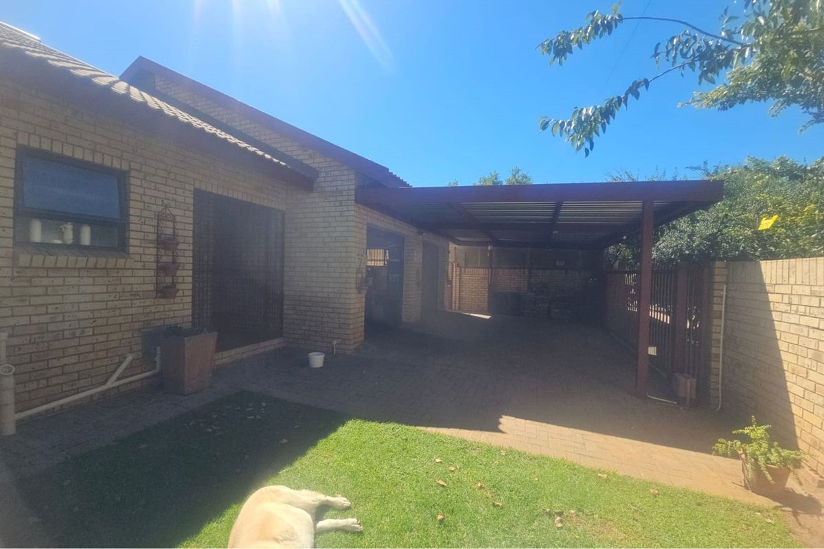A rear exterior view featuring a brick facade, a paved driveway area, and a covered carport structure adjacent to a small lawn.
