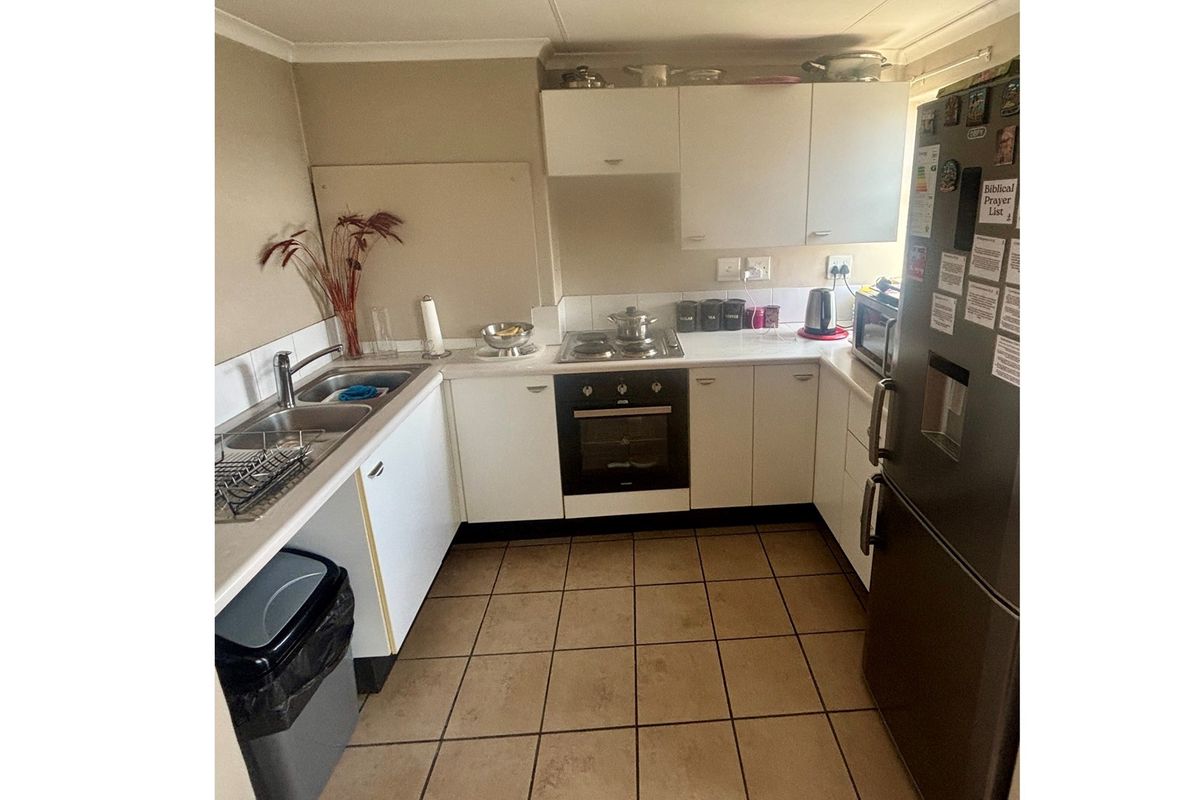 Compact kitchen featuring white cabinetry, built-in oven, hob, and double sink with tiled flooring.