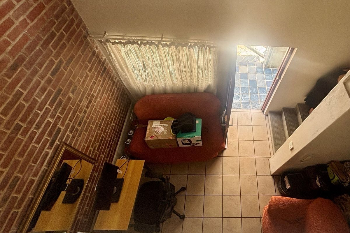 An elevated view of a living area featuring a distinctive exposed brick feature wall, tiled flooring, and direct access to an outdoor patio space.