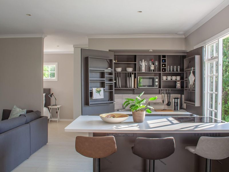 Modern open-plan living area featuring a compact kitchen with built-in cabinetry, integrated appliances, and a central island with a cooktop.