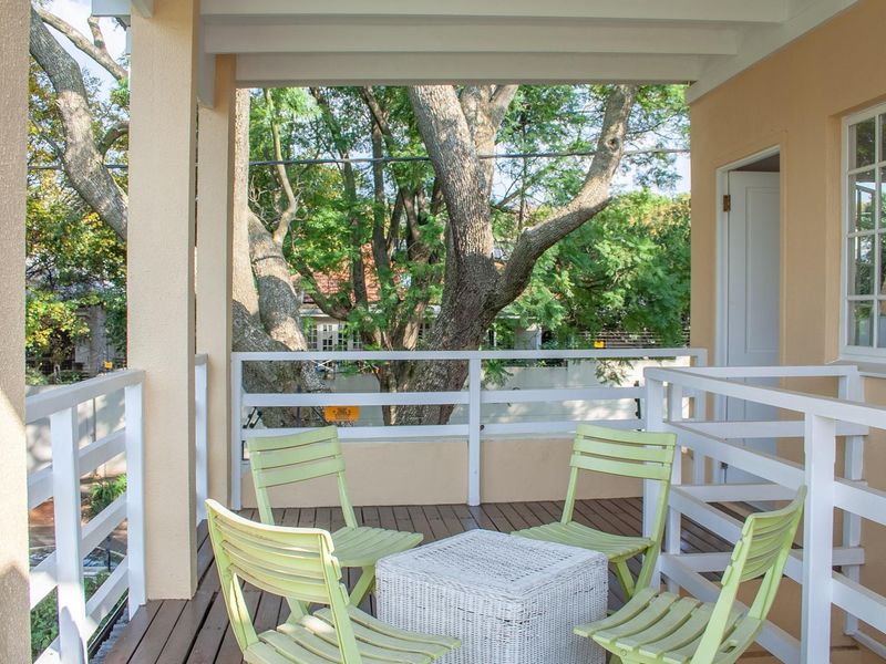 A covered balcony featuring timber decking and white timber balustrades, offering a pleasant outdoor seating area with views of the surrounding trees.