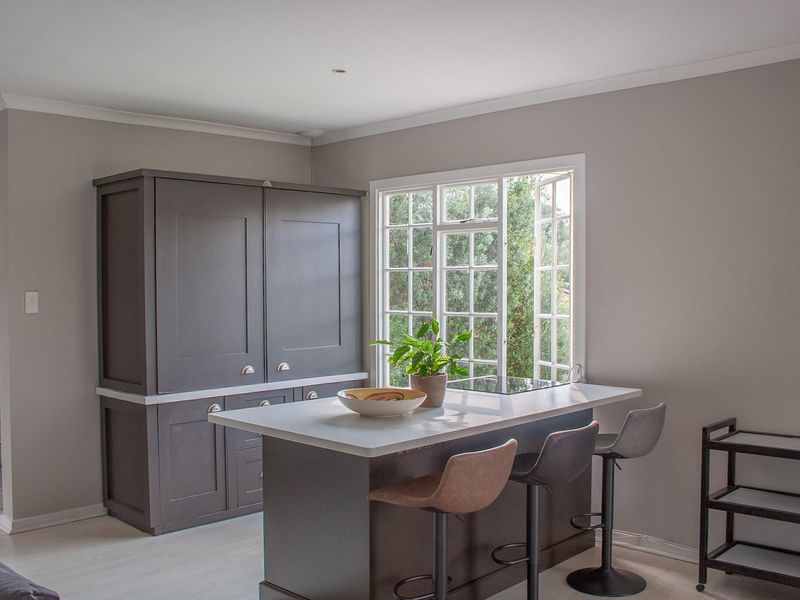 A modern kitchen featuring dark grey cabinetry, a central island with a stone countertop, and a large window providing natural light.