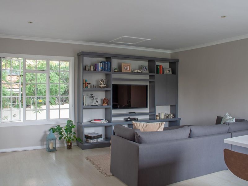 A well-maintained living room featuring a large built-in grey shelving unit, recessed lighting, and light-toned laminate flooring with natural light from the window.