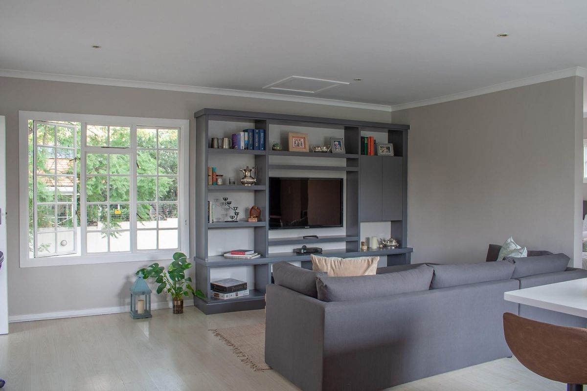 A well-maintained living room featuring a large built-in grey shelving unit, recessed lighting, and light-toned laminate flooring with natural light from the window.
