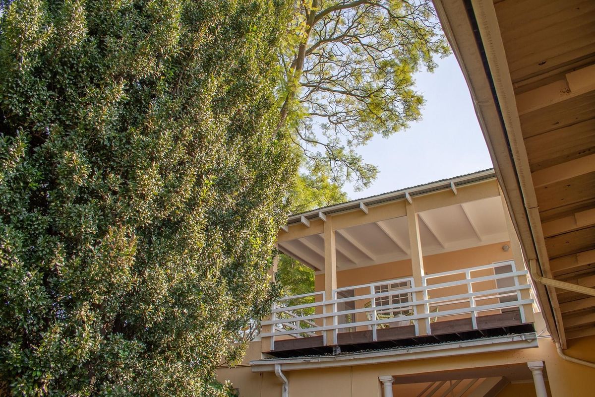 A view of the cottage's rear elevation featuring a raised timber deck with white balustrades, set against mature garden foliage.