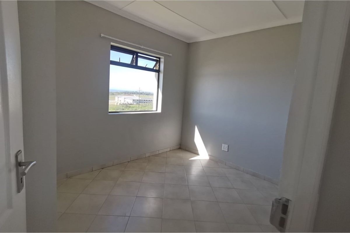 A clean, empty bedroom featuring neutral grey walls, tiled flooring, and a window providing natural light and exterior views.
