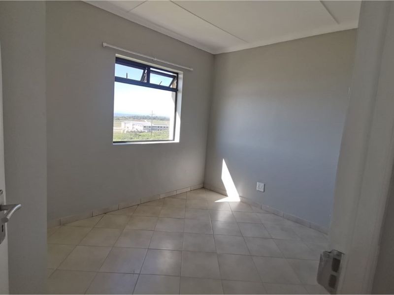 A clean, empty bedroom featuring neutral grey walls, tiled flooring, and a window providing natural light and exterior views.