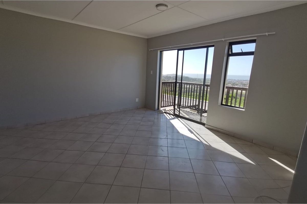 An empty, neutrally painted living area featuring tiled floors, a sliding glass door, and a window with natural light and exterior views.